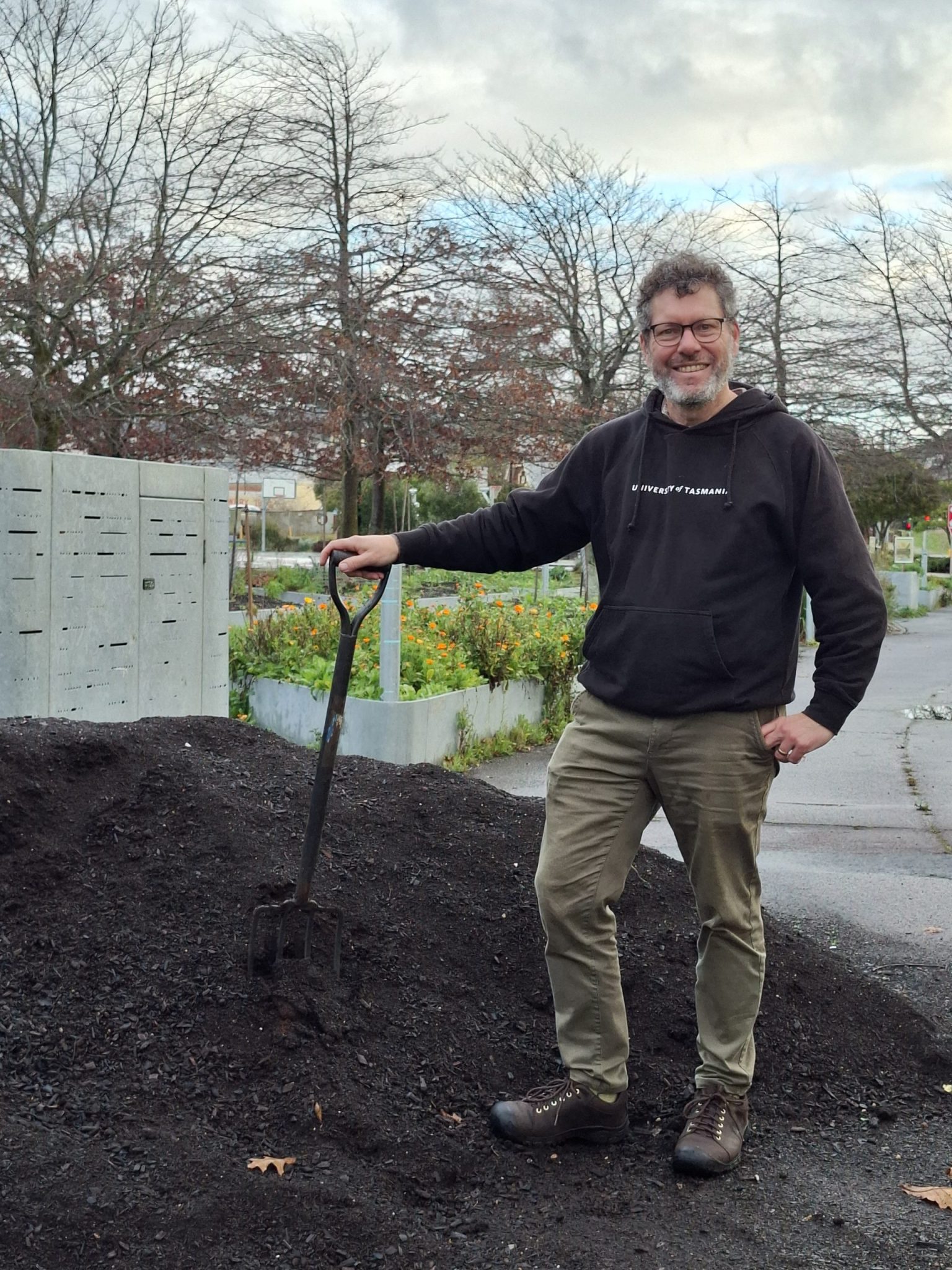 A man stand with a gardening fork next to a large pile of compost