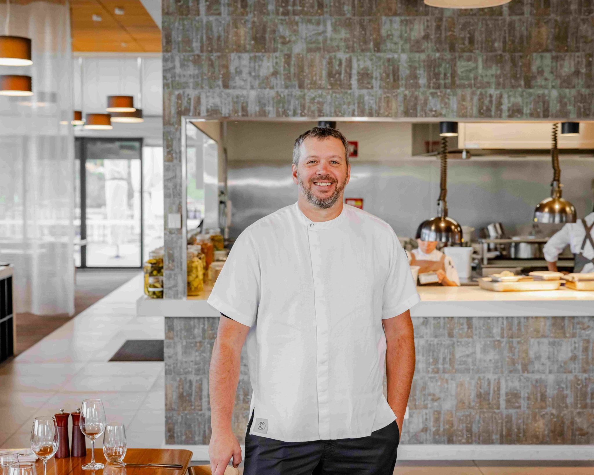 Chef Thomas stands in a restaurant with the kitchen behind him