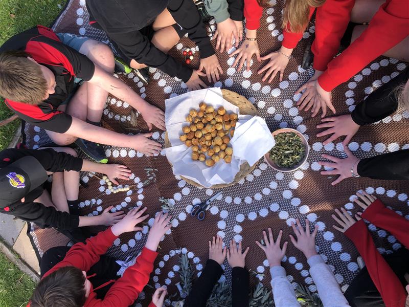 Children gathered seated on a mat with their hands in the centre of the mat.
